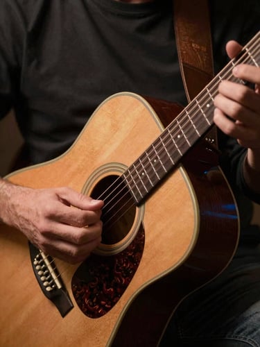 Tight close-up of hands playing an acoustic guitar under warm amber stage lighting, deep charcoal background.