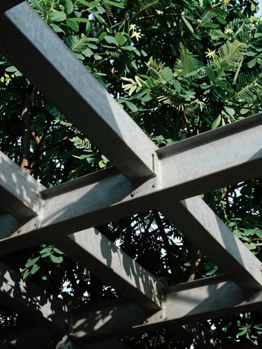 Low-angle architectural crop of interlocking steel and concrete beams under sharp daylight, deep forest green shadows, high contrast, 35mm lens
