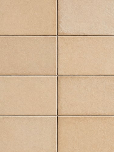 Close-up architectural photograph of perfectly aligned large-format ceramic tiles on a wall, sharp grout lines, warm sand tones, natural side lighting highlighting the flat surface, 35mm.