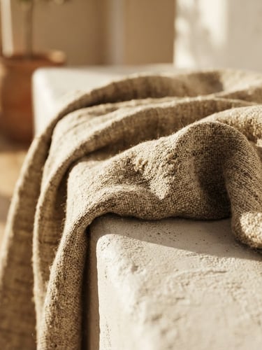 Macro photograph of heavy-weight oatmeal linen fabric draped over a low-profile plaster bench, warm afternoon sunlight casting deep textures and soft shadows
