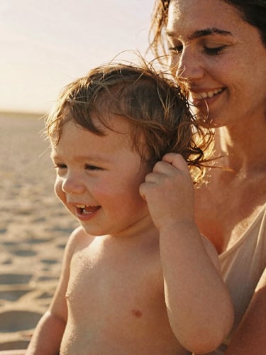 Intimate close-up of a mother laughing as her toddler pulls her hair, warm golden hour sun backlighting them, soft sand tones, 35mm film texture