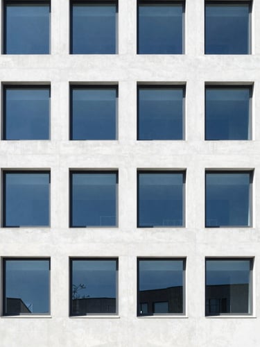 Minimalist architectural detail of a modern institutional concrete facade with structured geometric windows, bright high-key natural daylight, crisp shadows, deep blue accents, 35mm