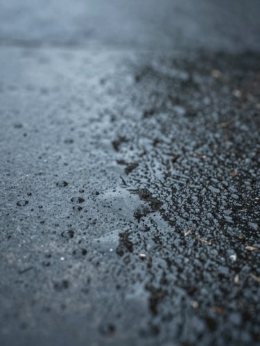 Extreme macro shot of rain on dark stone, soft diffused overcast daylight, moody shadows, minimalist composition