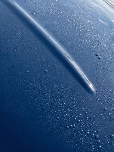 Close-up of water beading perfectly on a freshly treated deep blue gelcoat surface, bright morning sun creating high-contrast highlights, crisp editorial marine photography.