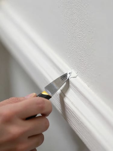 Close-up macro shot of a painter in a clean uniform applying a perfect paint edge against white timber trim with precision tape