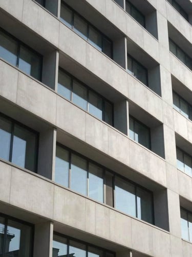 Architectural close-up of a modern healthcare facility facade, clean geometric lines, bright daylight with sharp slate-gray shadows.