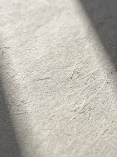 Macro close-up of heavy embossed cotton paper stock showing raw, tactile fibers under sharp low-angle sunlight casting deep architectural shadows.