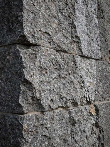 A vertical portrait of a massive hand-chiseled granite foundation wall, deep mortar joints catching dramatic side lighting, overcast natural daylight, raw stone textures.