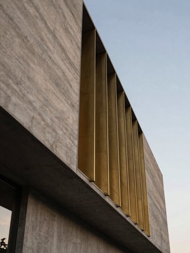 Low-angle architectural shot of a modern concrete and brass facade, dramatic twilight lighting emphasizing physical textures and structural solidity, negative space on the right.