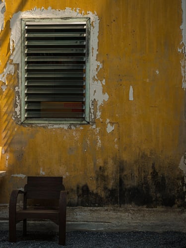 Une chaise disposée devant un mur de couleur jaune avec une grille d'aération défraichie.