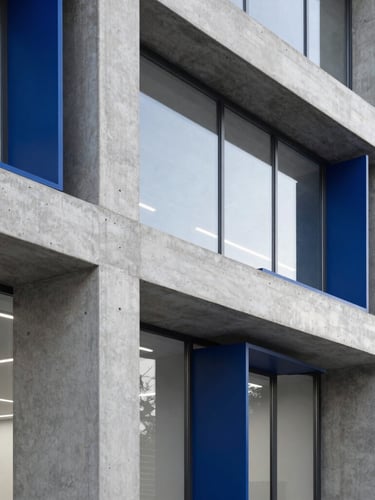 Crisp editorial photography of a modern, minimalist architectural office with concrete structures, natural window light, and deep blue accents, 50mm lens.