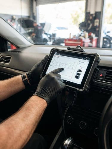 Clean, modern diagnostic tablet plugged into a car dashboard, bright natural Australian daylight, high-contrast shadows, 50mm lens, mechanic's hands visible.