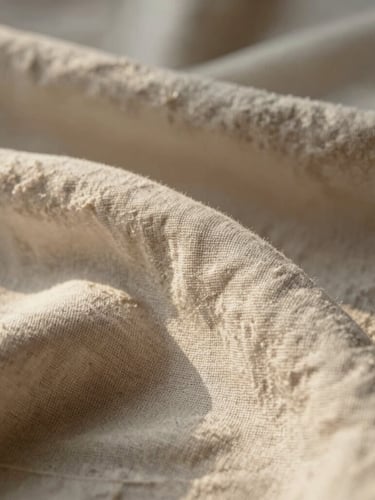 Macro photograph of soft organic linen folds under warm morning light, creating gentle shadows and a sense of absolute stillness.