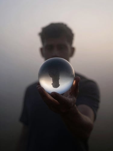 A figure partially obscured by dense morning mist, low-contrast twilight, soft-focus silhouette holding a glass sphere that refracts light.