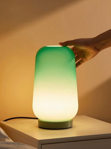 A hand adjusting a modern glowing green sculptural lamp on a bedside table, warm ambient light, cozy room, 35mm lens.