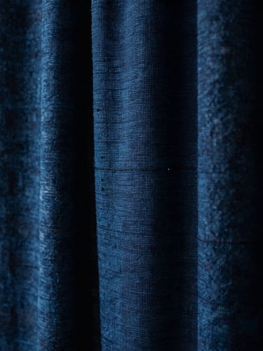 Tight macro shot of hand-loomed indigo textiles showing rich mineral-dyed grain and heavy weave, dramatic low-key window lighting.