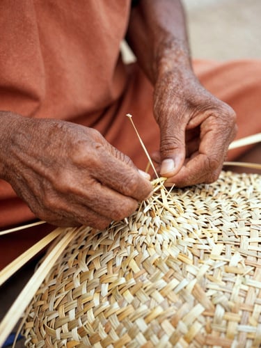 Artisan hands weaving a traditional straw basket, close-up focus on the intricate texture and natural fibers, warm clay tones
