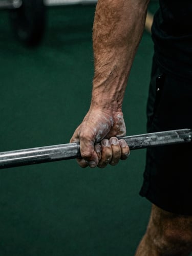Moody athletic photography, dramatic low-key lighting, close-up of a heavily chalked hand gripping a steel barbell, deep forest green and matte black tones, high contrast, 35mm film