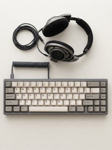 A crisp, isolated mechanical keyboard and premium headphones on an off-white, subtly textured neutral background, sharp studio lighting, geometric overhead angle.
