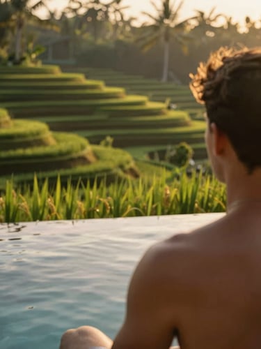 Candid over-the-shoulder view of a traveler looking out at a lush green infinity pool overlooking Ubud rice terraces at sunrise, warm golden light