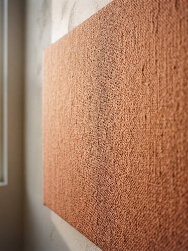A close-up of a fabric soundproof panel in soft terracotta catching raking side-light in a minimalist room, medium format film