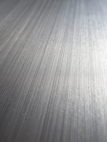 Extreme close-up of a brushed steel surface, studio strobe lighting raking across the grain at a low angle, tight crop revealing micro-texture and parallel tool marks, no subject other than the material itself, wide negative space toward the right edge
