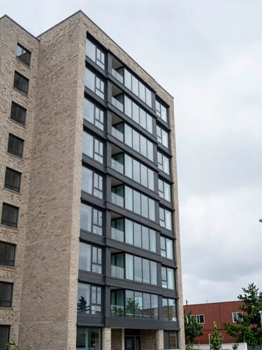 Wide exterior view of a mid-rise residential property facade in natural overcast daylight, building centered slightly left with open sky to the right, clean brick and glass surfaces, no people, documentary framing