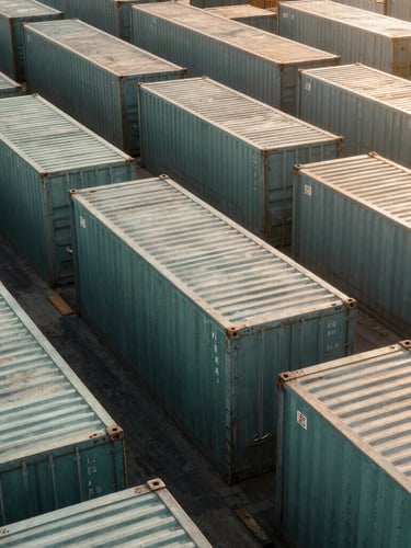 High-angle architectural view of a modern, structured port with industrial steel containers, sharp daylight, geometric symmetry, desaturated emerald and warm sand tones, bleed.
