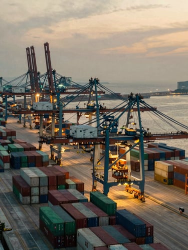 High-angle architectural view of a modern, automated port terminal at dusk, showing vast container stacks and illuminated gantries, sharp contrasting light, wide-angle, geometric symmetry, desaturated emerald and warm sand tones, cinematic.