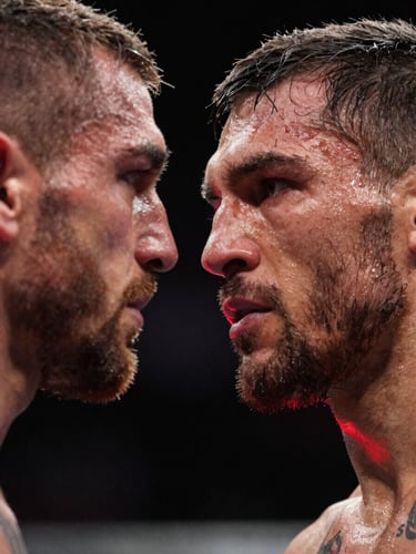 Tight close-up on a UFC fighter's face under the harsh octagon ring lighting, sweat on the brow, eyes locked on the opponent, high-contrast shadows, red corner light catching the jaw, no crowd visible — pure intensity and focus