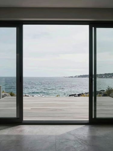 Expansive sliding glass doors with a flush threshold, opening to a coastal deck