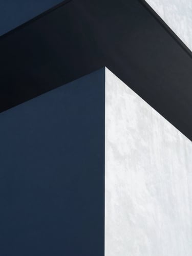 A minimalist editorial portrait of a founder in a modern architectural setting, shot from a low angle with cool crisp daylight, deep navy shadows, and clean geometric lines, 35mm lens.