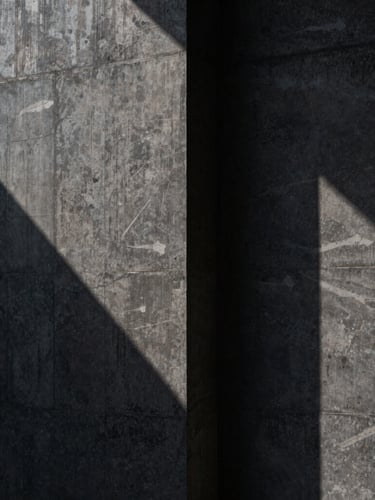 Abstract close-up of a monolithic dark concrete wall with sharp brutalist shadows, cast in low-key side-lighting, solid and secure.