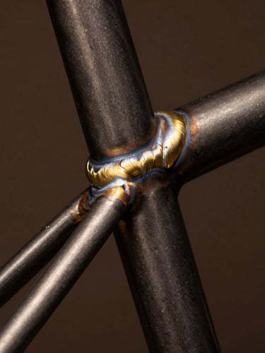 Extreme close-up of a clean brass fillet weld on a dark steel bicycle frame, dramatic studio spotlighting, shallow depth of field, 35mm