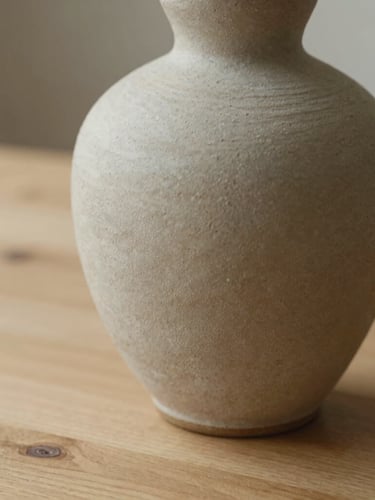 A tactile close-up of a textured ceramic vase on a raw wooden table, soft natural daylight casting gentle warm shadows, 35mm lens, shallow depth of field