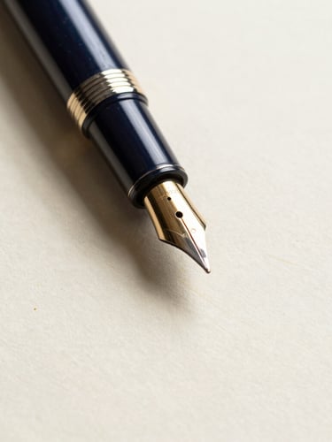 Macro close-up of high-end fountain pen resting on structured cream paper with subtle gold leaf embossing, soft dramatic shadows, warm daylight, 35mm