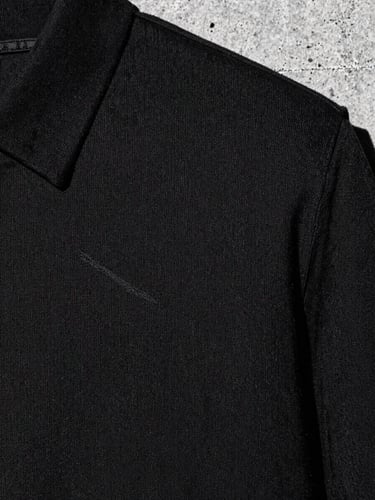 Close-up crop of heavy-weight black cotton fabric texture with clean embroidery, raw urban concrete background, high-contrast monochrome