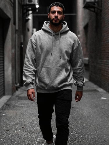 Low-angle candid shot of a man walking down a raw urban alleyway at night, wearing a heavy steel-grey hoodie, moody low-key lighting