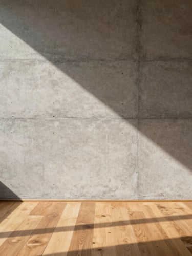 Flat-on architectural crop of a raw concrete wall meeting warm oak floorboards, hard afternoon sun casting a sharp diagonal shadow, unposed human scale, architectural monograph style.
