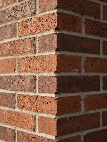 Close-up detail of a brick wall corner junction, two bond patterns meeting at a precise external angle, soft north-facing daylight raking across the mortar joints, no people, no staging