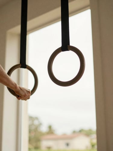 Close-up of hands gripping wooden calisthenics rings hanging in a domestic doorway, soft overcast daylight, natural fitness photography.