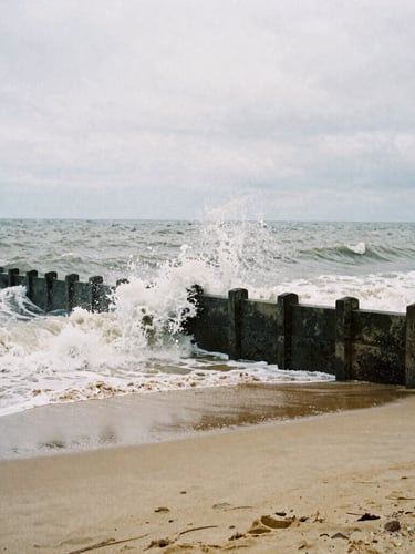 Moody film photography of the overcast Margate coastline, raw sea-navy waves crashing against concrete sea walls, desaturated sand tones, high contrast, 35mm