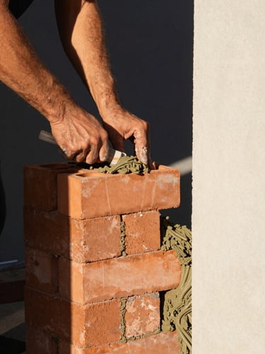 Tight graphic close-up of structural terracotta bricks and wet mortar being laid by a mason under natural high-contrast sunlight, sharp architectural framing, 35mm