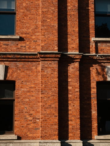 A close-up of a historic red brick facade with sharp architectural shadows under high-contrast natural sunlight, 35mm warm editorial photography