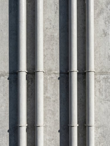 Symmetrical vertical conduit runs along a textured concrete wall, clean industrial shadows, straight-on architectural framing.