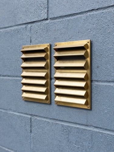 A close-up of clean, modern brass subfloor vents neatly installed into a heritage double-brick wall, bright daylight, sharp commercial photography.