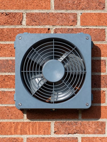 Sharp commercial photography of a clean, modern underfloor extraction fan installed neatly in a heritage red brick foundation wall, bright daylight, 35mm lens.
