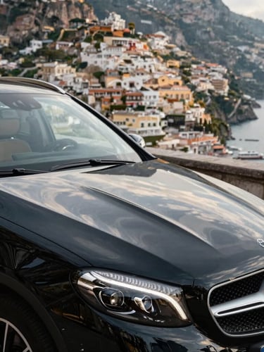 Close-up of a gleaming black Mercedes-Benz executive vehicle parked on a scenic coastal curve overlooking Positano, warm sun glinting off the polished hood.