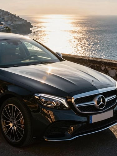 Close-up of a gleaming black Mercedes-Benz executive sedan parked on a quiet cliffside turn in Positano, warm golden hour light reflecting off the deep blue Mediterranean sea in the background, elegant and clean composition.