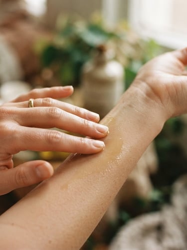 Close-up of hands gently applying botanical oils to skin, soft diffused warm daylight, shallow depth of field, natural textures.